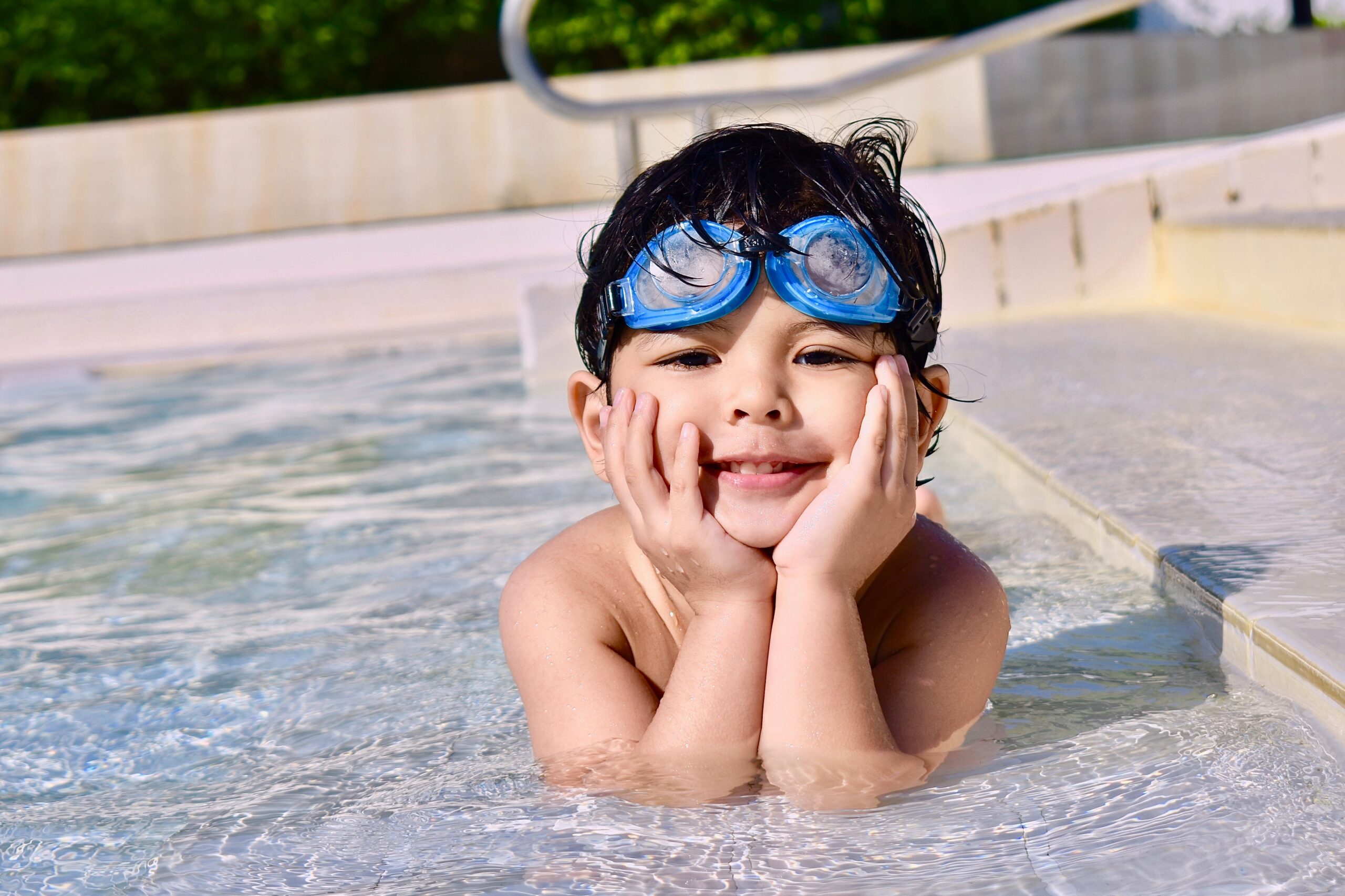 boy smiling in pool with goggles on owasso living blog summer pool gear