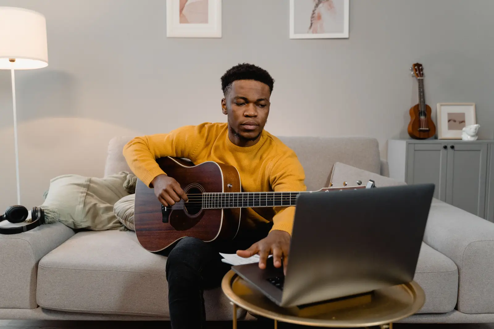 Man playing guitar while using a laptop in his living room Man playing guitar while using a laptop in his living room